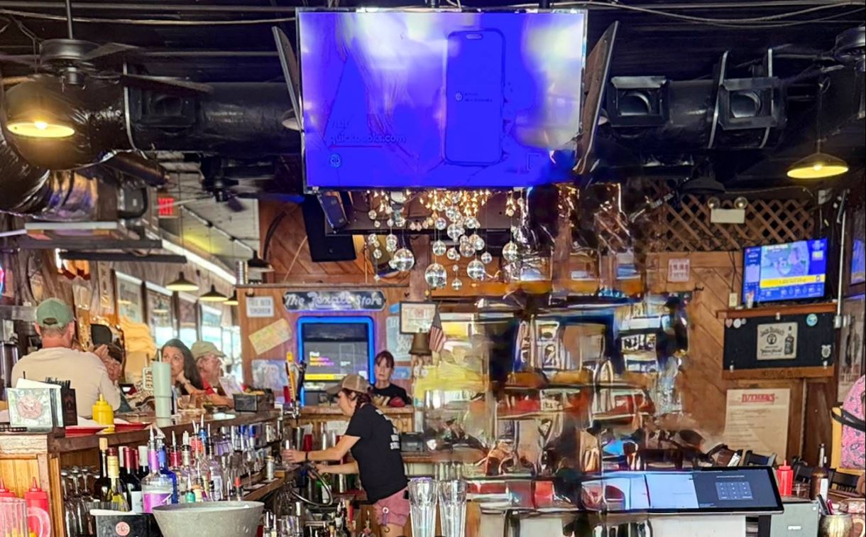 Inside Luther's Rare and Well Done bar with TVs, string lights, and bartender serving customers